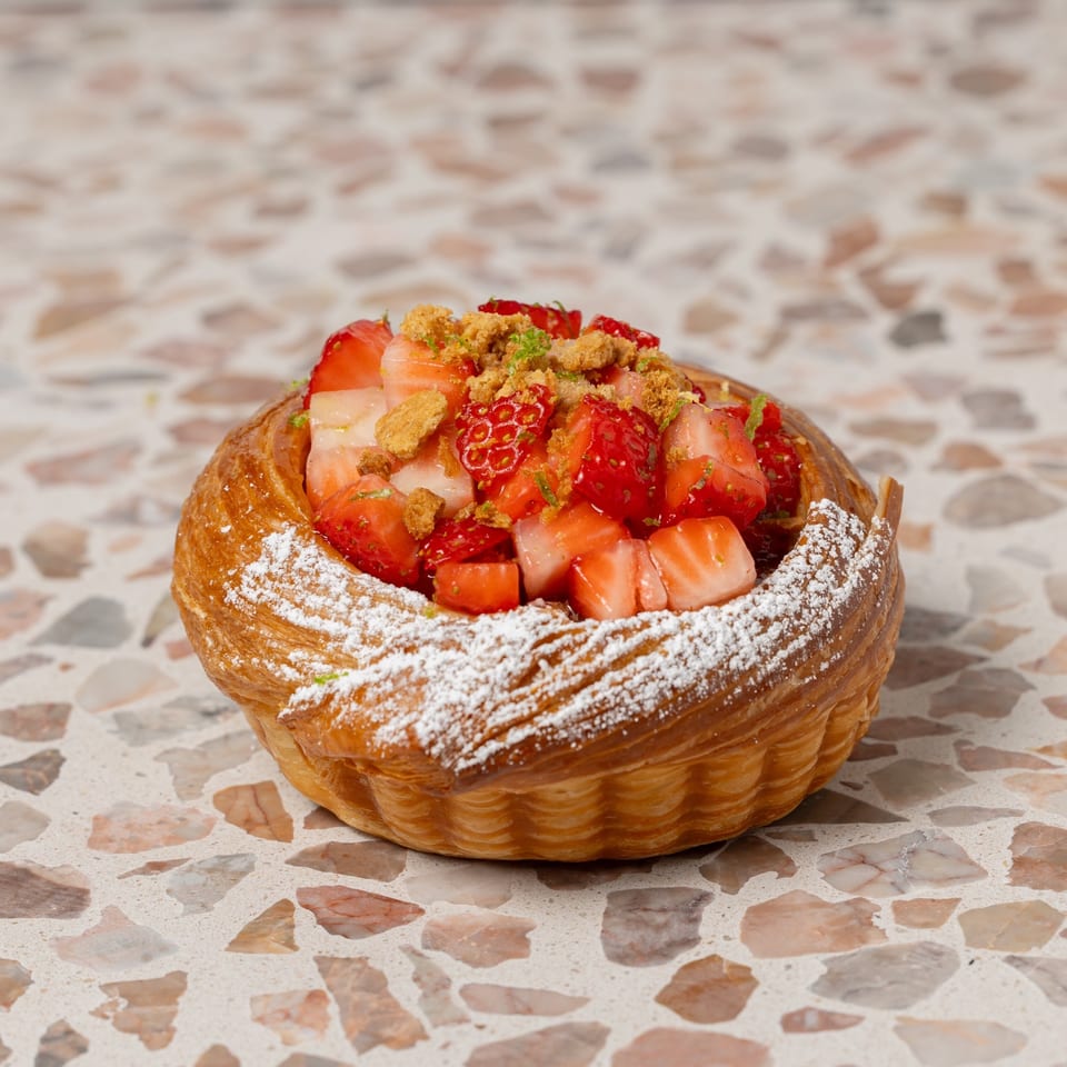 Pastry filled with sliced strawberries, topped with crumble and powdered sugar, displayed on a terrazzo countertop.