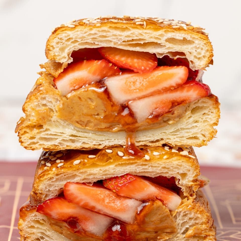 Stacked flaky pastries filled with sliced strawberries, creamy nut spread, and syrup, topped with sesame seeds.